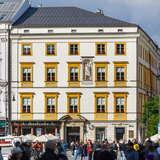 Bryłę budynku Pałacu Krzysztofory. Na pierwszym planie tłum osób przechadzające się po Rynku Głównym w Krakowie.