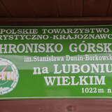 Zielona tablica z nazwą schroniska PTTK na Luboniu Wielkim, logo Polskiego Towarzystwa Turystyczno-Krajoznawczego i wysokością 1022 m n.p.m.