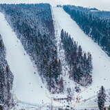 Widok z drona na cały stok narciarski Sport Arena Myślenice. Stok otaczają zimowe, ośnieżone choinki.
