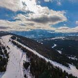Zdjęcie z drona na trasy zjazdowe ośrodka narciarskiego Jurgów-Ski. Ośnieżone trasy, drzewa iglaste, a z tyłu widok na lekko zakryte chmurami Tatry.