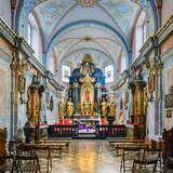 Ołtarz w Kościele św. Mikołaja w Krakowie. Kolorowe wnętrze kościoła, z malowidłami na ścianach i suficie oraz złotymi elementami. Przed ołtarzem znajduje się kilka ławek i krzeseł do siedzenia dla wiernych.