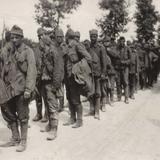 Zdjęcie archiwalne, czarno-białe. Kolumna żołnierzy idących drogą.