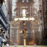 Złoty krzyż, w tle wnętrze kościoła ze stallami i ołtarzem.