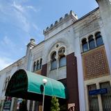 Front budynku łaźni w stylistyce mauretańskie widoczny zza zielonej markizy przed wejściem.