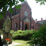 Po prawej fronton kościoła, z przodu drzewa i figura świętego.